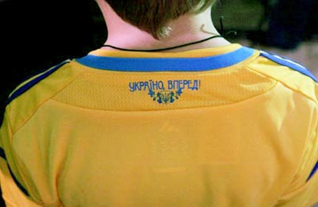 На задней стороне воротниковой канвы футболки расположен национальный герб и лозунг: «Украина, вперед!»